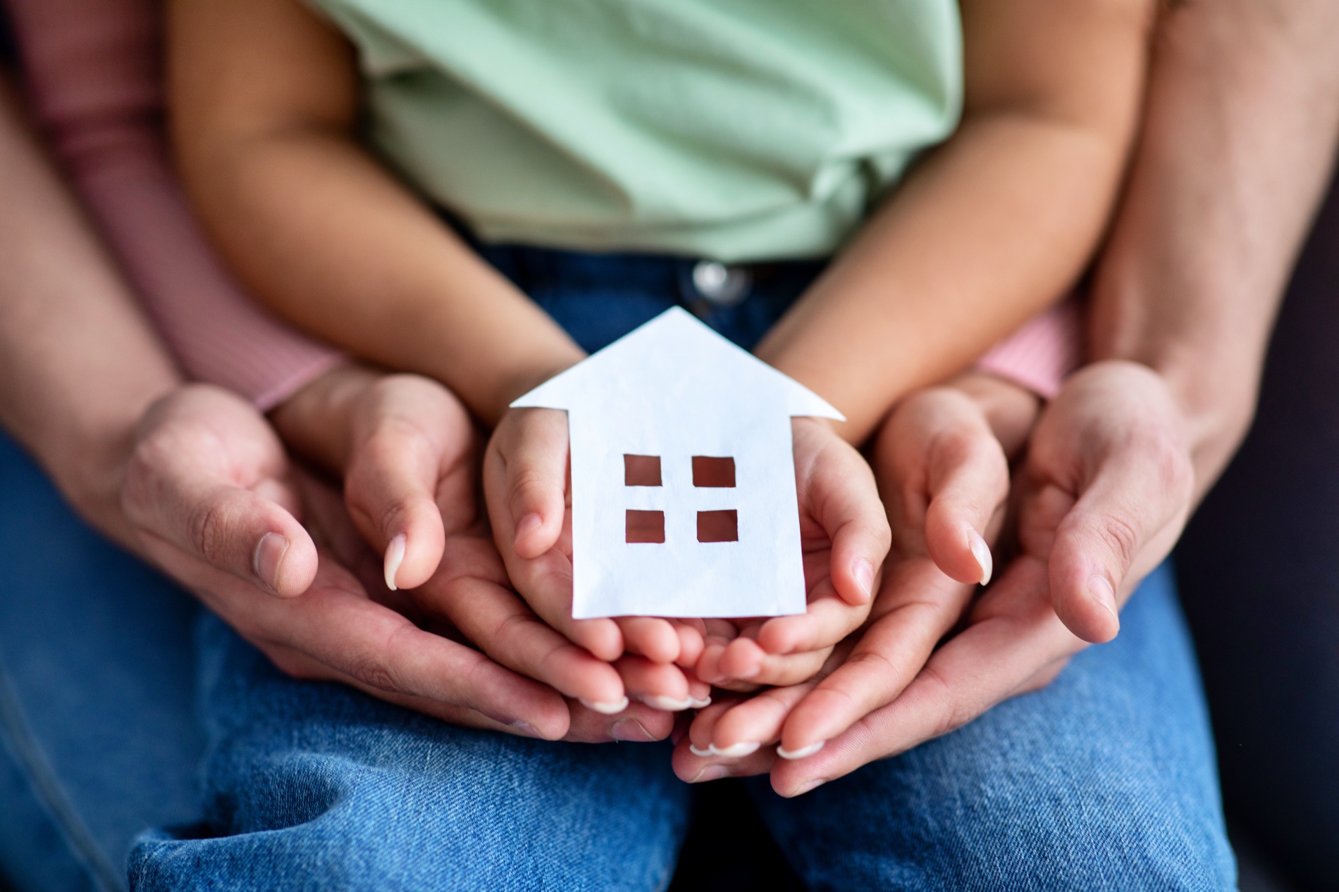 Husband, wife, and child holding a cutout paper house in their hands.