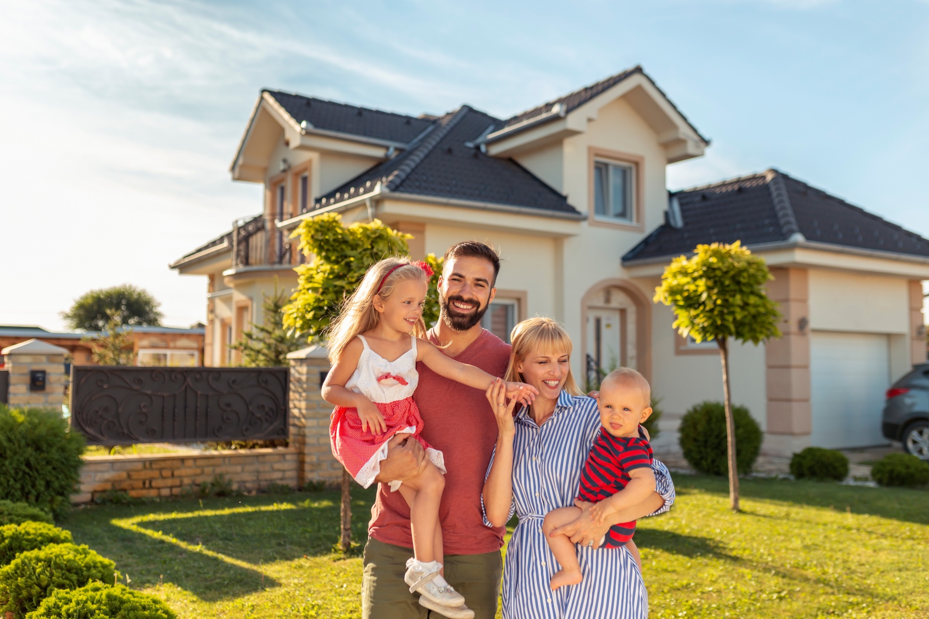 Happy family, mother and father, with their two children in front of a beautiful home.