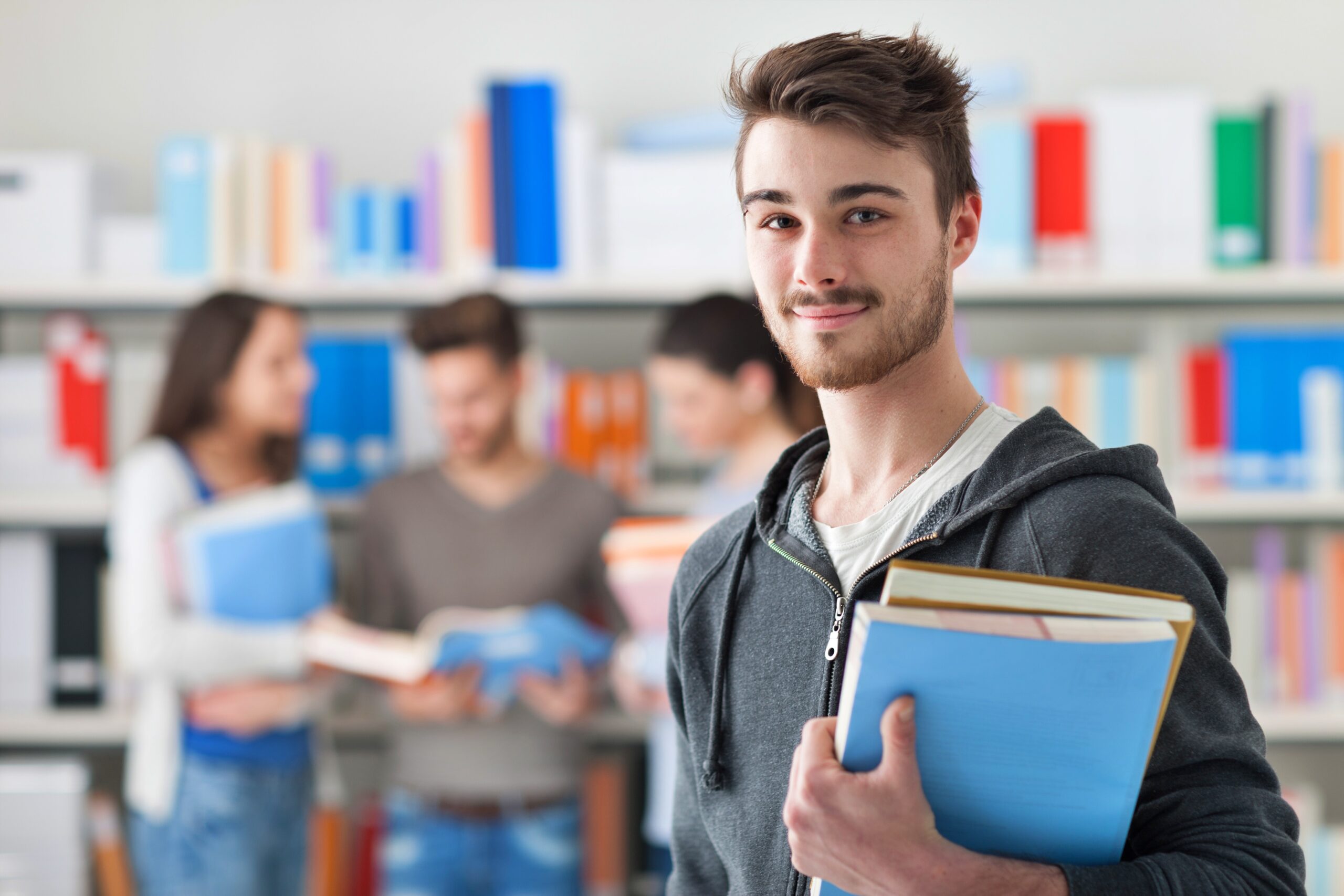 Male student holding books in a library.