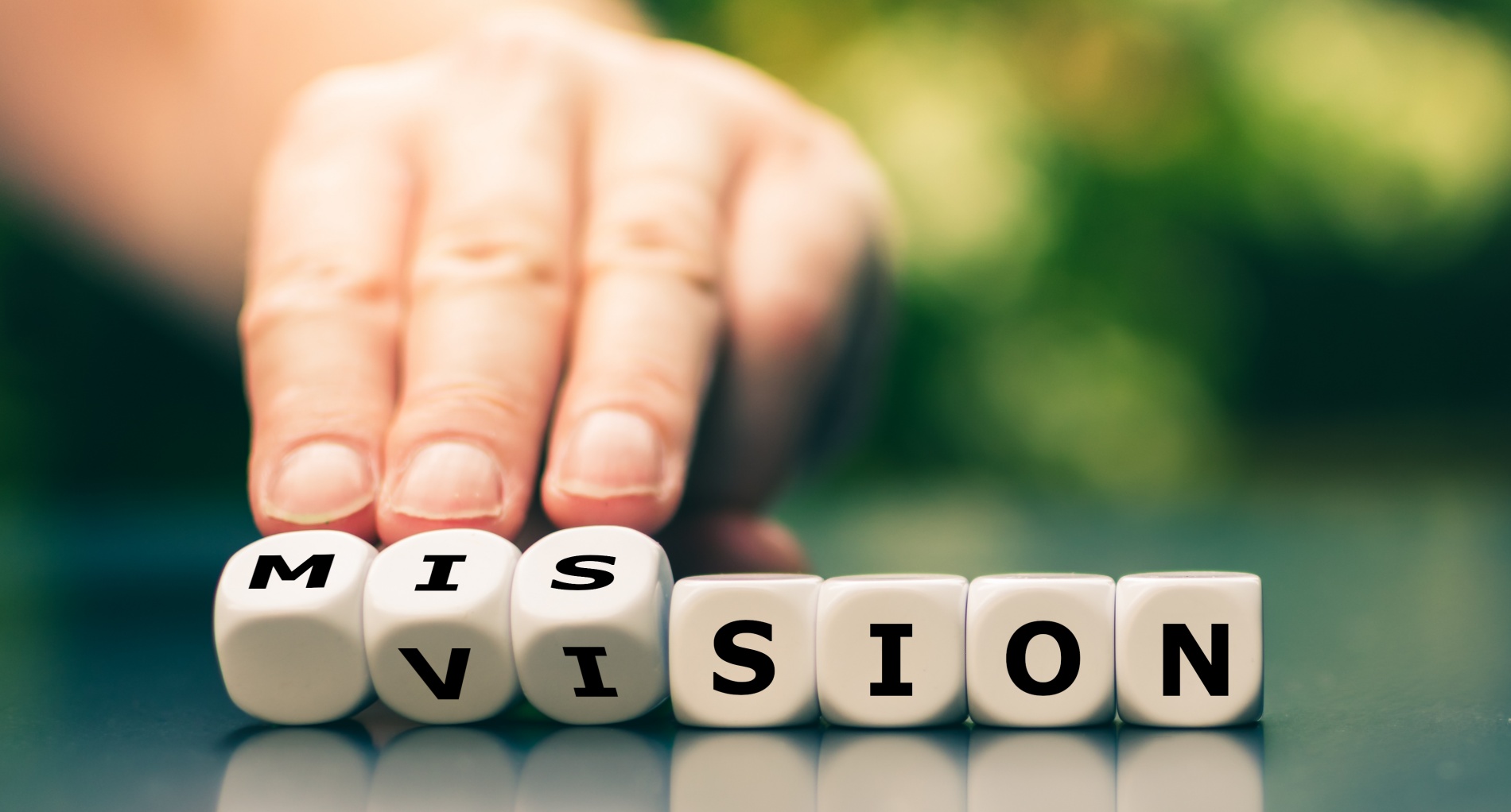 Hand turns dice and changes the word vision to mission.